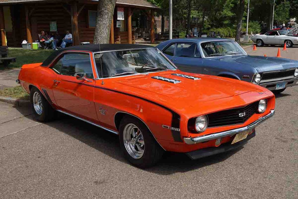 Front view of a bright orange 1969 Chevrolet Camaro SS with black vinyl roof at a classic car show.