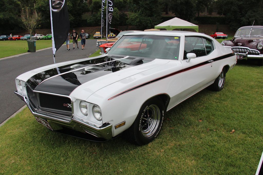 1970 Buick GSX 455 Coupe in Apollo White with black hood stripe and red accent lines at a classic car show