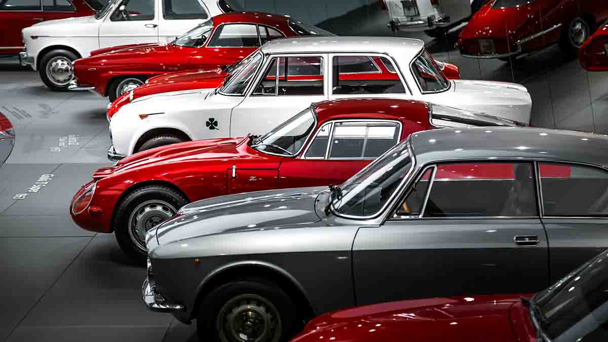 Three sisters standing next to classic cars inside barn